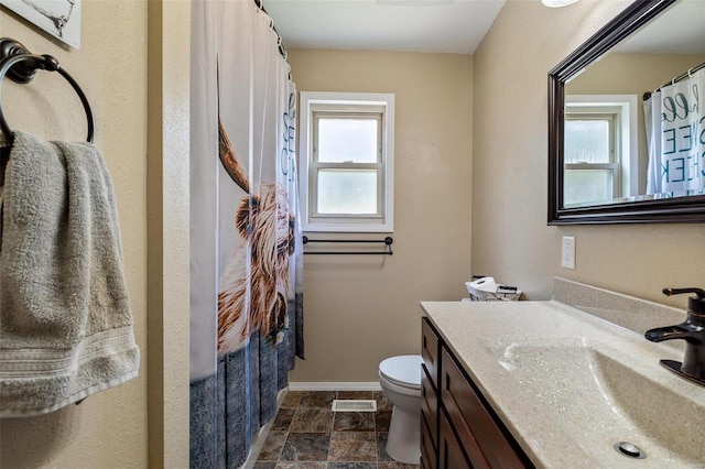 bathroom with a wealth of natural light, stone finish flooring, baseboards, and vanity