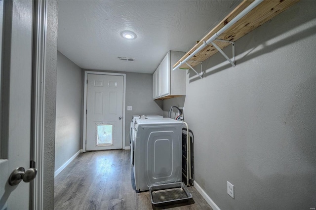 laundry room with a textured ceiling, cabinets, separate washer and dryer, and hardwood / wood-style floors