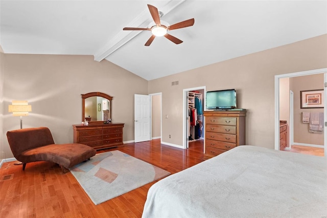 bedroom featuring ensuite bath, ceiling fan, vaulted ceiling with beams, hardwood / wood-style floors, and a walk in closet