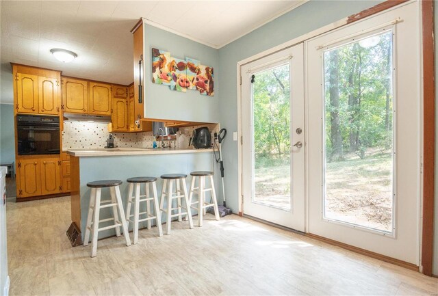 kitchen featuring a kitchen breakfast bar, oven, backsplash, french doors, and kitchen peninsula