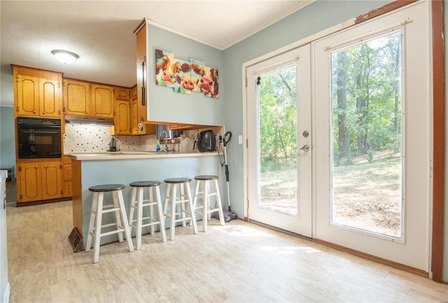 kitchen with french doors, light countertops, backsplash, black oven, and a kitchen bar