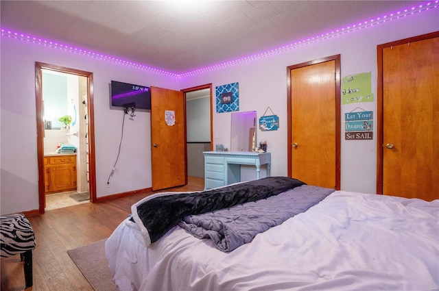 bedroom with ensuite bath, baseboards, and hardwood / wood-style floors