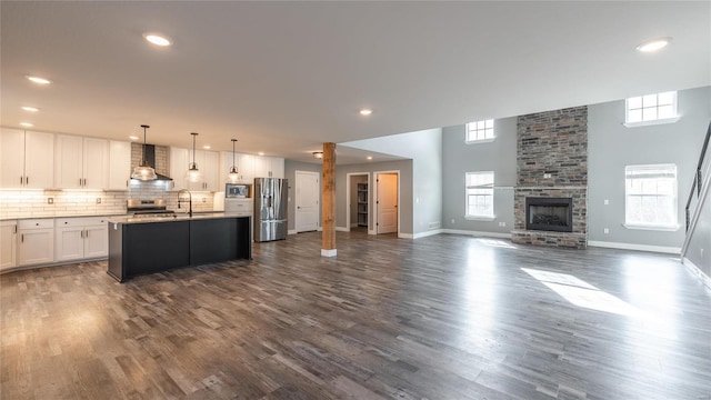 kitchen featuring white cabinetry, a center island with sink, pendant lighting, stainless steel appliances, and wall chimney range hood