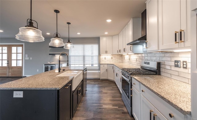 kitchen with wall chimney exhaust hood, white cabinetry, decorative light fixtures, stainless steel appliances, and a kitchen island with sink