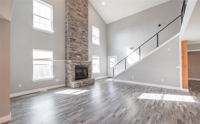 unfurnished living room with wood-type flooring, a brick fireplace, and a towering ceiling