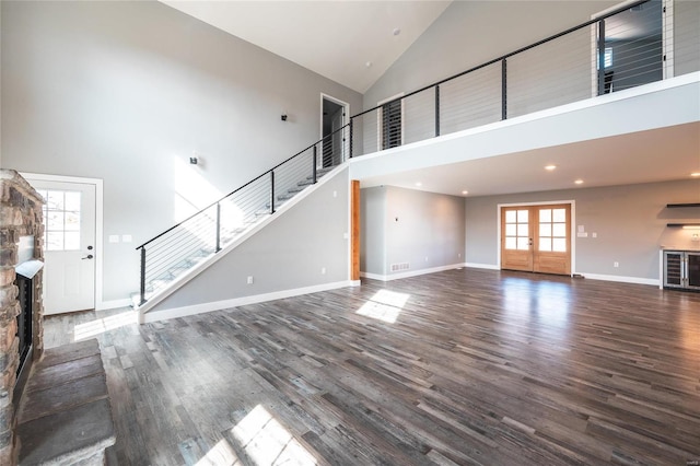 unfurnished living room featuring dark hardwood / wood-style flooring, a stone fireplace, high vaulted ceiling, and french doors