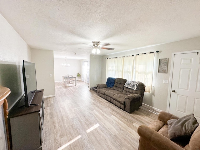 living room featuring ceiling fan with notable chandelier, a textured ceiling, and light hardwood / wood-style flooring