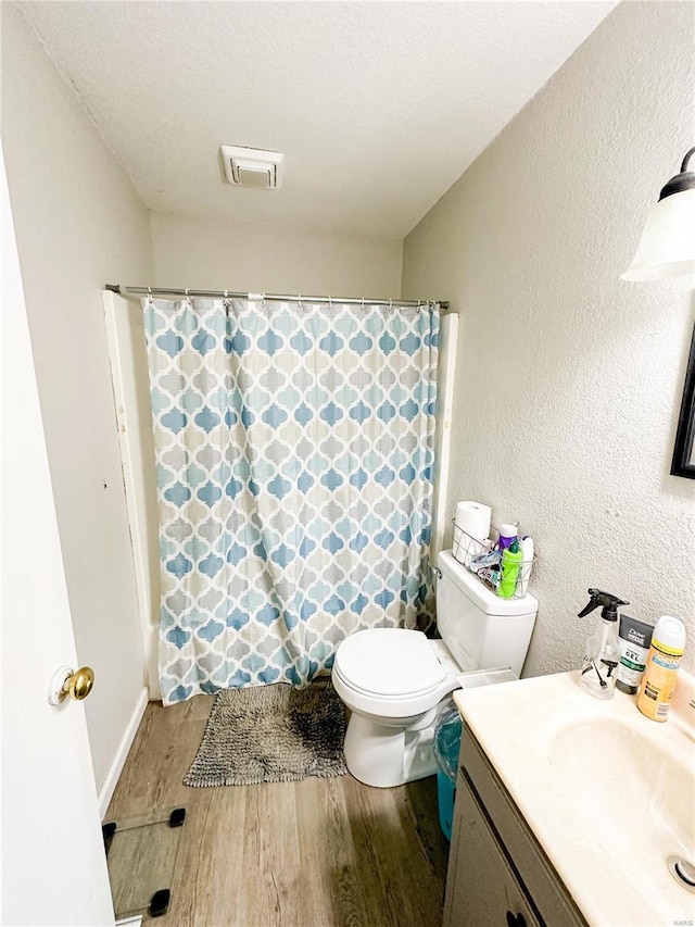 bathroom with a textured ceiling, vanity, walk in shower, toilet, and hardwood / wood-style flooring