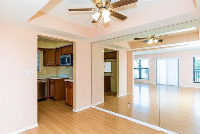 kitchen featuring light wood-type flooring, a raised ceiling, stainless steel appliances, and ceiling fan