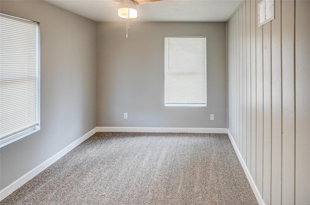 carpeted empty room featuring ceiling fan, a healthy amount of sunlight, and wood walls