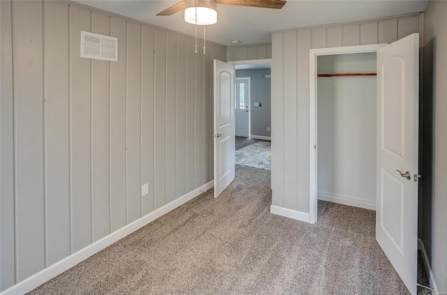 unfurnished bedroom with a closet, ceiling fan, wood walls, and carpet