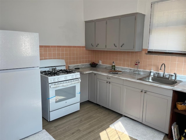 kitchen featuring gray cabinetry, backsplash, white appliances, light wood-type flooring, and sink