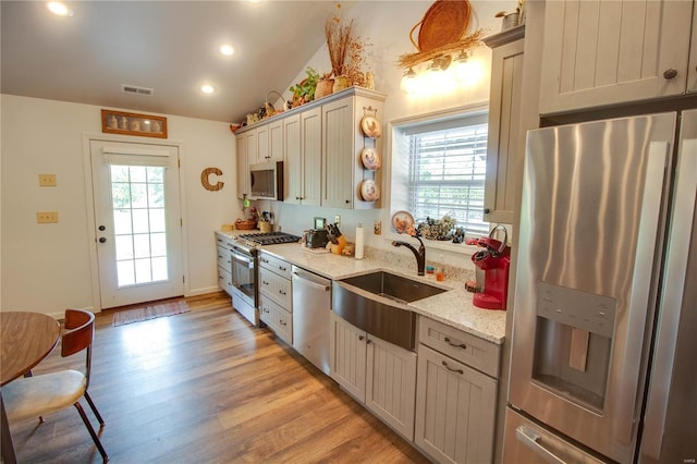 kitchen with light stone counters, stainless steel appliances, light hardwood / wood-style floors, sink, and lofted ceiling