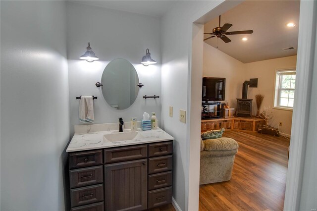 bathroom with hardwood / wood-style flooring, a wood stove, lofted ceiling, ceiling fan, and vanity