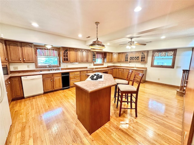 kitchen with a center island, light countertops, brown cabinetry, light wood-style floors, and white appliances