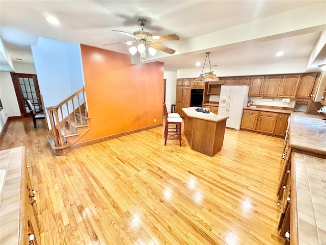 kitchen with white appliances, brown cabinetry, a center island, light countertops, and light wood-style floors