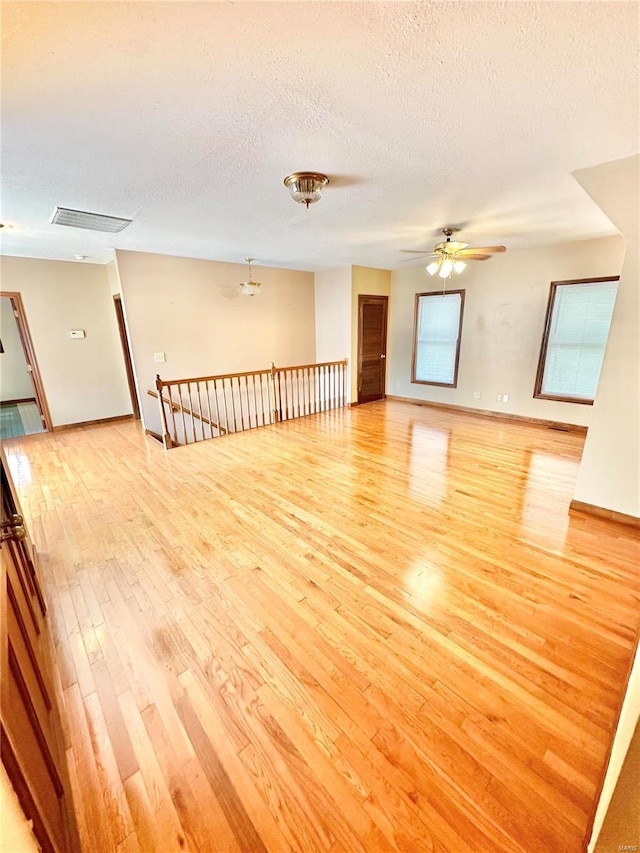 unfurnished room featuring a textured ceiling, ceiling fan, visible vents, baseboards, and light wood-type flooring