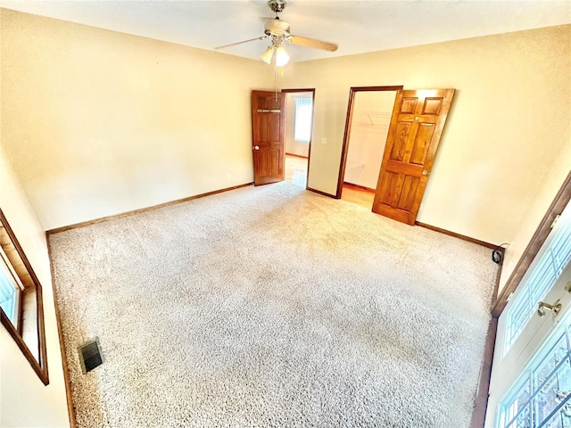 unfurnished bedroom with light carpet, baseboards, a walk in closet, and a ceiling fan