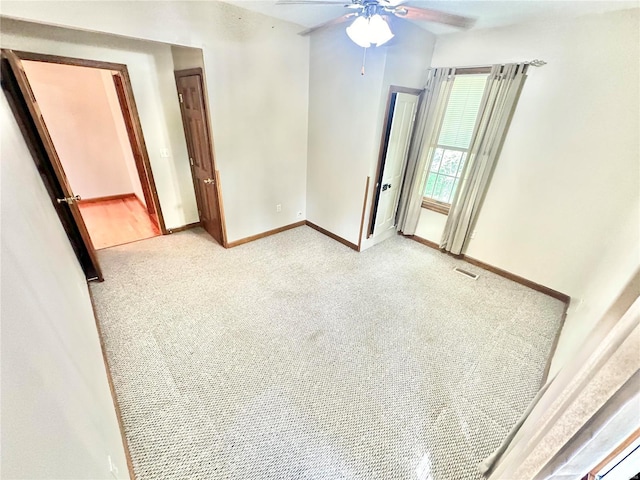 empty room featuring light carpet, a ceiling fan, visible vents, and baseboards