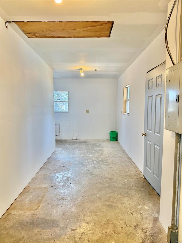 interior space featuring unfinished concrete flooring, attic access, and electric panel