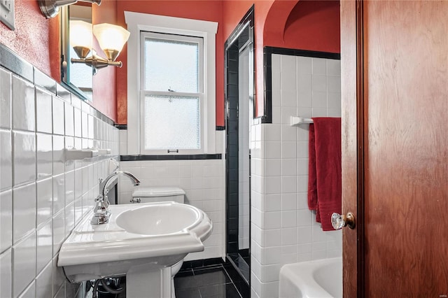 bathroom featuring a bathing tub, sink, tile patterned flooring, toilet, and tile walls