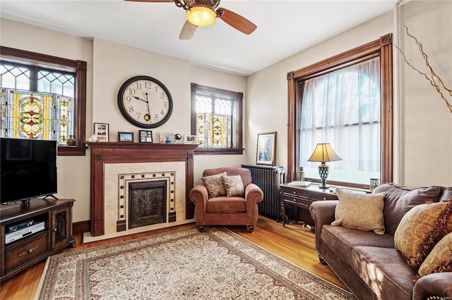 sitting room featuring a tile fireplace, light hardwood / wood-style floors, a wealth of natural light, and ceiling fan