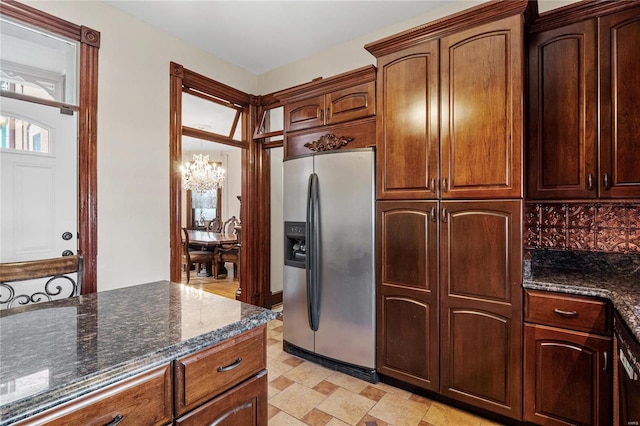 kitchen with stainless steel fridge, backsplash, dark stone counters, and a chandelier