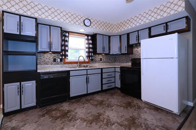 kitchen with gray cabinetry, light stone countertops, black appliances, backsplash, and sink