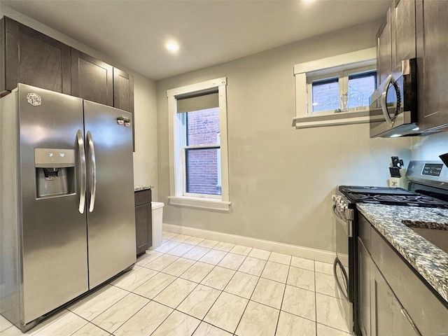 kitchen featuring dark brown cabinetry, stainless steel appliances, and dark stone countertops