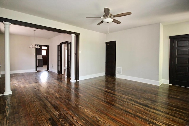 empty room with ornate columns, dark hardwood / wood-style floors, and ceiling fan with notable chandelier