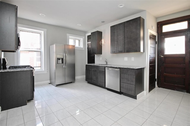 kitchen featuring dark brown cabinets, sink, light tile patterned flooring, appliances with stainless steel finishes, and light stone counters