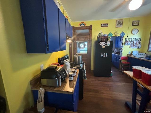 kitchen featuring stove, dark wood-type flooring, black refrigerator, ceiling fan, and blue cabinetry