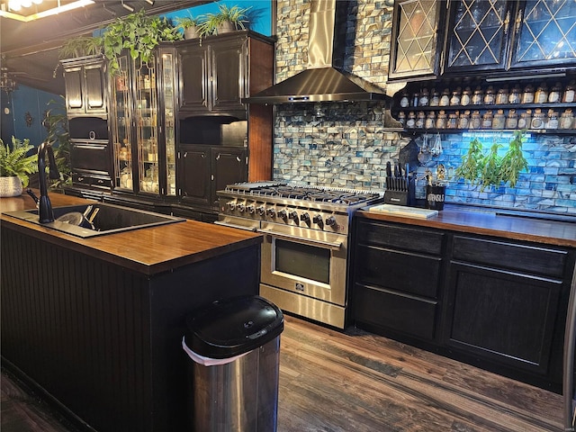 kitchen featuring stainless steel stove, wooden counters, dark wood-type flooring, a sink, and wall chimney exhaust hood