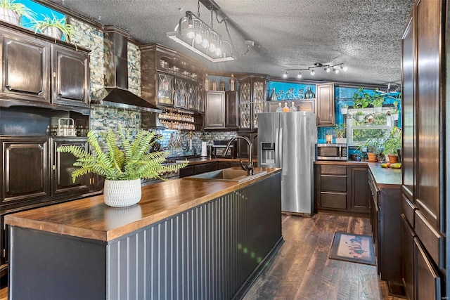 kitchen with a textured ceiling, wooden counters, appliances with stainless steel finishes, and wall chimney range hood