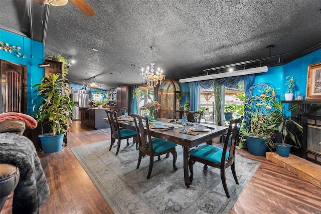 dining room with a textured ceiling, a glass covered fireplace, wood finished floors, and track lighting