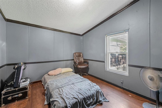 bedroom with crown molding, vaulted ceiling, a decorative wall, and wood finished floors