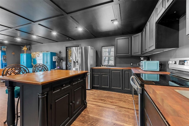 kitchen featuring stainless steel appliances, a kitchen island, a kitchen breakfast bar, wooden counters, and light wood-type flooring