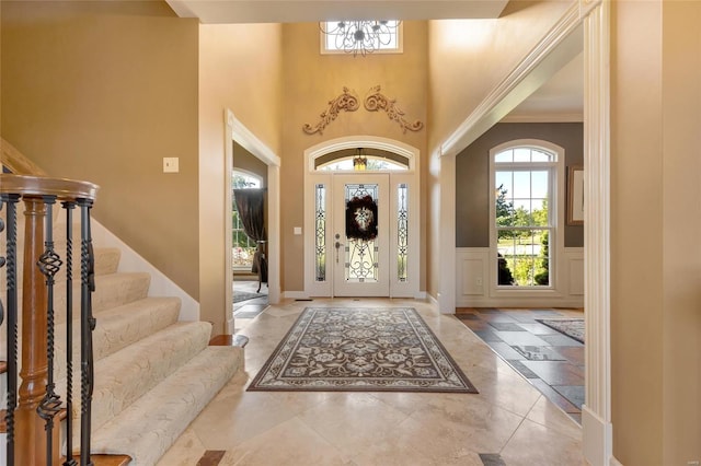 entryway with a wainscoted wall, an inviting chandelier, stairs, a high ceiling, and a decorative wall