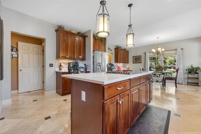 kitchen with a chandelier, stainless steel appliances, light countertops, brown cabinets, and pendant lighting