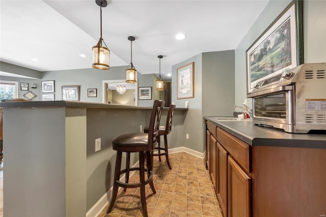 kitchen with a breakfast bar, a sink, brown cabinets, dark countertops, and pendant lighting