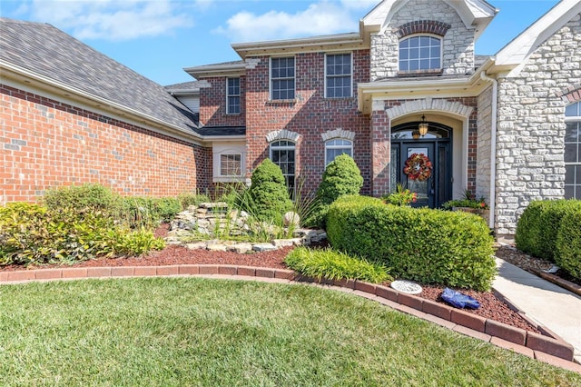 traditional home featuring a shingled roof, stone siding, brick siding, and a front lawn