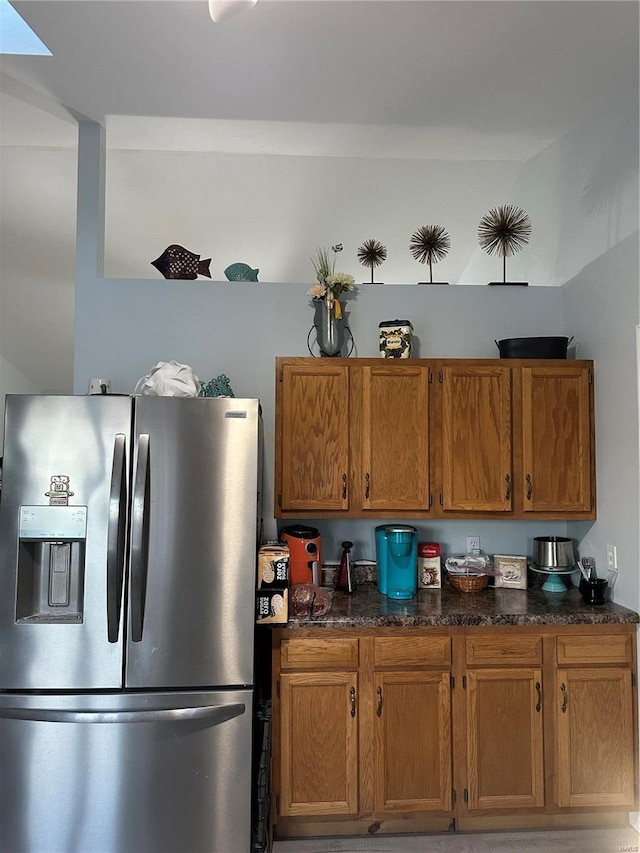 kitchen featuring dark stone countertops, stainless steel fridge, and brown cabinets