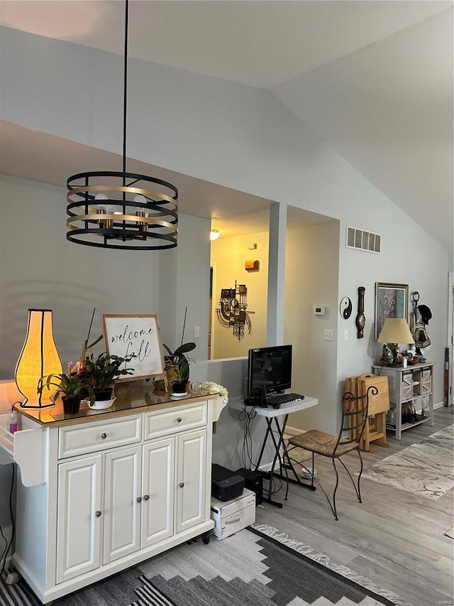 interior space with visible vents, a notable chandelier, wood finished floors, white cabinets, and vaulted ceiling