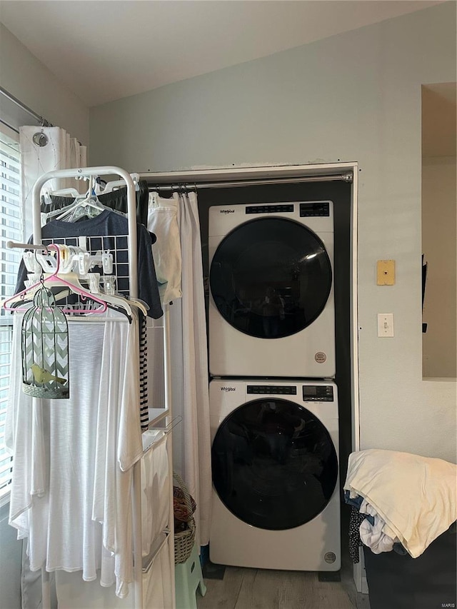 washroom featuring stacked washer / drying machine, wood finished floors, and laundry area