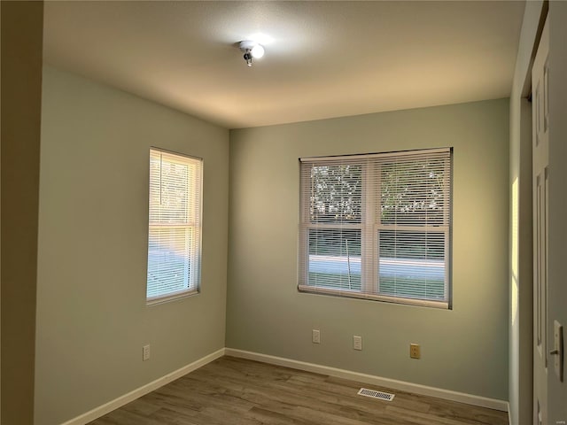 unfurnished room with wood finished floors, a healthy amount of sunlight, visible vents, and baseboards