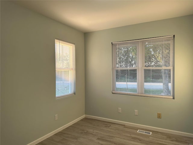 spare room featuring visible vents, a healthy amount of sunlight, baseboards, and wood finished floors