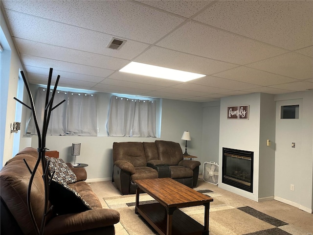 living room with a drop ceiling, baseboards, light colored carpet, and a glass covered fireplace