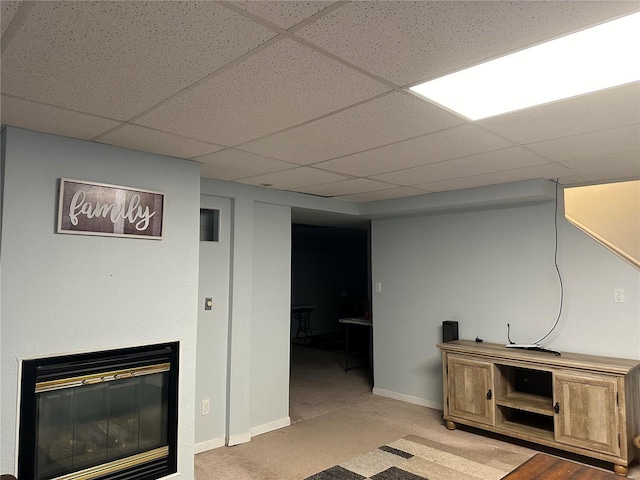 finished below grade area featuring a glass covered fireplace, baseboards, and a drop ceiling