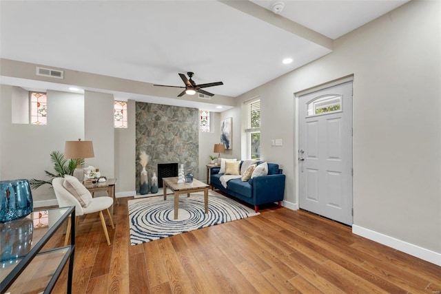 living room featuring a large fireplace, ceiling fan, and wood-type flooring