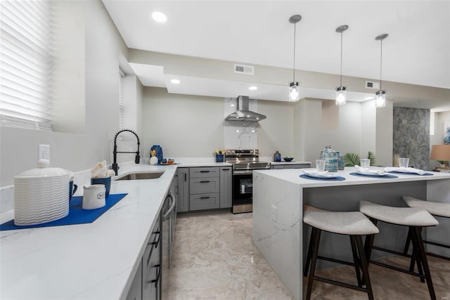 kitchen with wall chimney exhaust hood, pendant lighting, appliances with stainless steel finishes, a breakfast bar, and sink